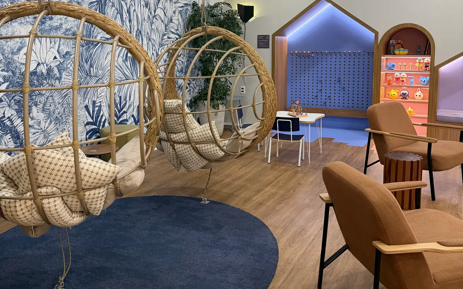 Sala de espera do consultório no Market Place, Morumbi: cadeiras-balanço de palha, tapete azul e espaço de brincar ao fundo
